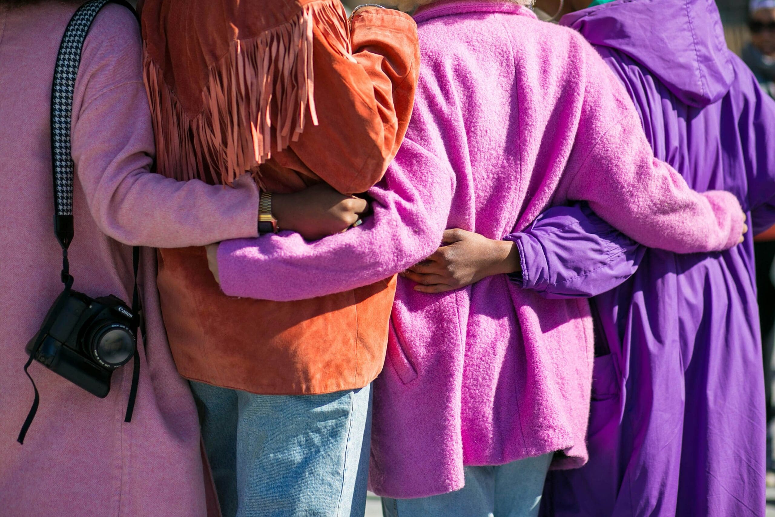 Group of people standing close with their arms around each other, wearing colorful coats, symbolizing connection, belonging, and compassionate community — representing Ominira Therapy’s trauma-focused and somatic approach in Nevada.