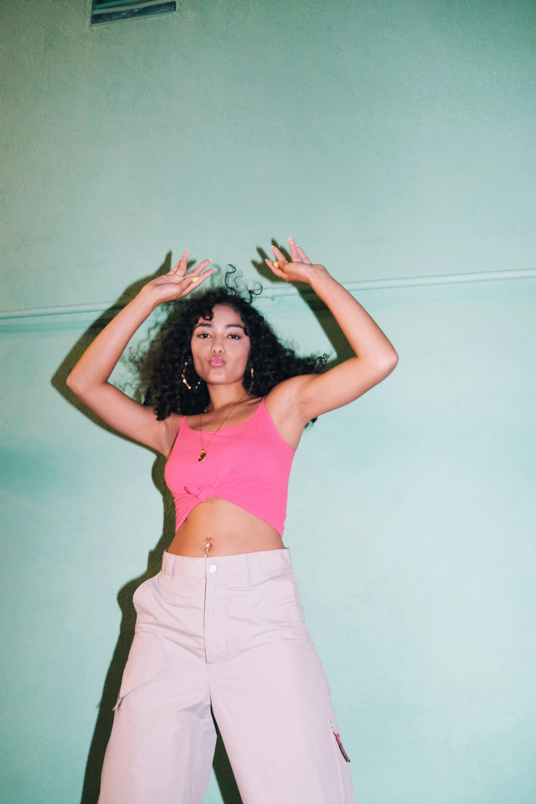 Woman with curly hair dancing confidently against a mint green wall, representing Ominira Therapy’s focus on somatic awareness, embodiment, and emotional expression as pathways to healing.
