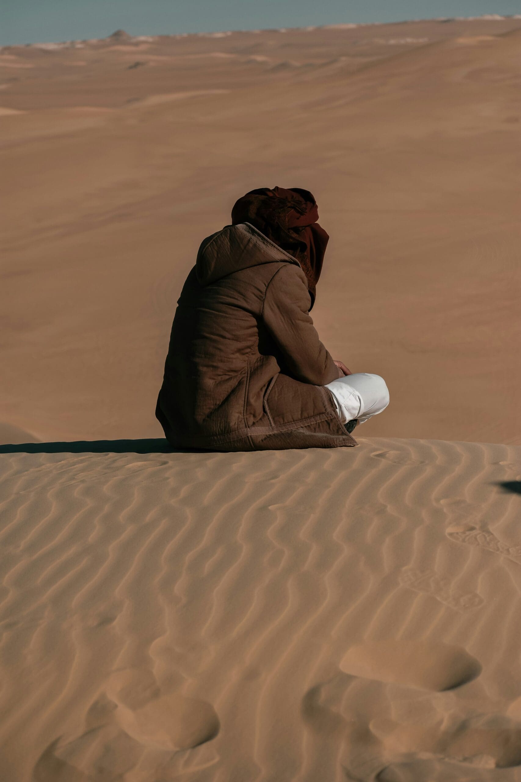 Person sitting on sand dunes in quiet desert landscape, representing Ominira Therapy’s approach to somatic awareness, grounded reflection, and trauma-focused healing through presence and embodiment.